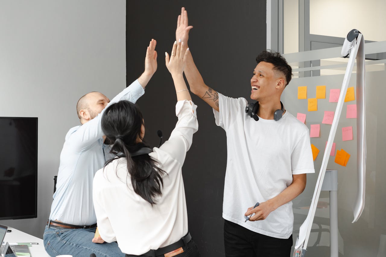 about-02 Diverse team members in an office high-fiving, symbolizing success and teamwork in a supportive environment.